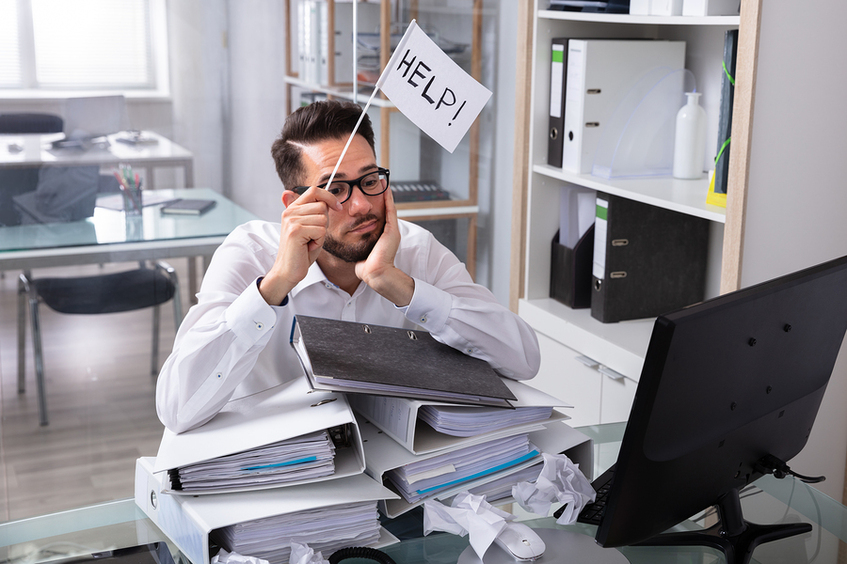 Man sitting at a desk with a pile of binders and a help flag.